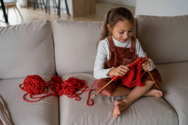 소파에 앉아서 집안에서 뜨개 질하는 법을 배우는 어린 소녀. — 스톡 사진
