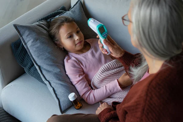 Grootmoeder zorgt voor haar zieke kleinkind liggend op de bank — Stockfoto