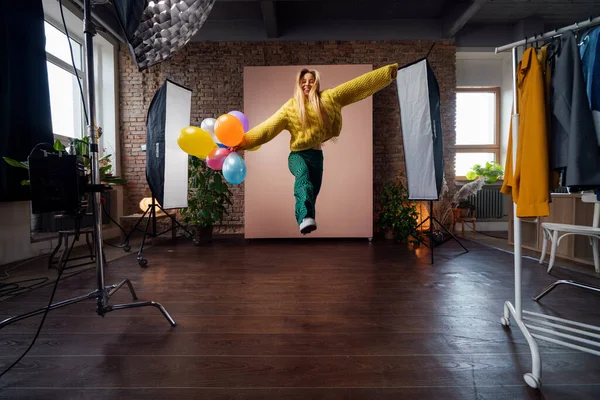 Модный студийный портрет счастливой молодой женщины с воздушными шарами, прыгающей, за кулисами фотосессии . — стоковое фото