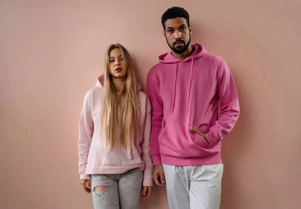 Mode studio porträtt av unga biracial par i hoodies poserar över rosa bakgrund. — Stockfoto