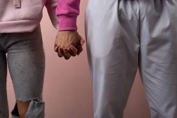 Close-up of young biracial couple holding hands over pink background. — Stock Photo, Image