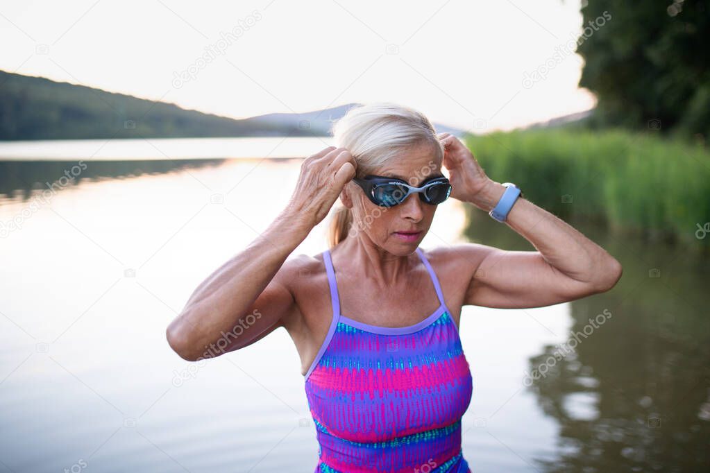 Portrait of active senior woman swimmer outdoors by lake.