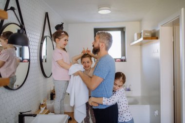 Father bonding with his three little daughters in bathroom, morning routine concept.