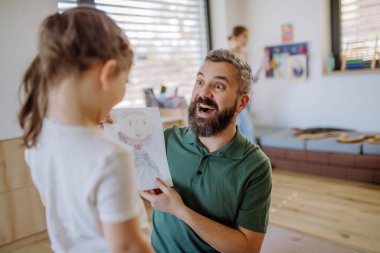Happy father getting drawings from his little daughter at home.