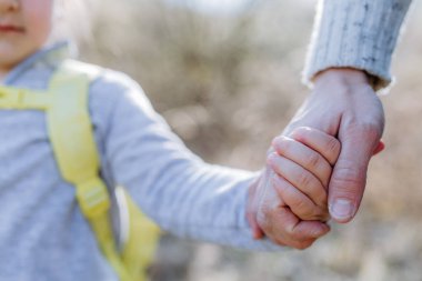 Father and daughter hold hands on walk in nature.