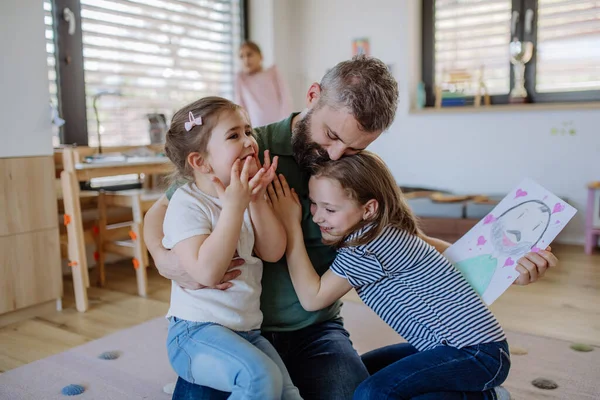 Padre di tre piccole figlie che ricevono disegni da loro a casa. — Foto Stock