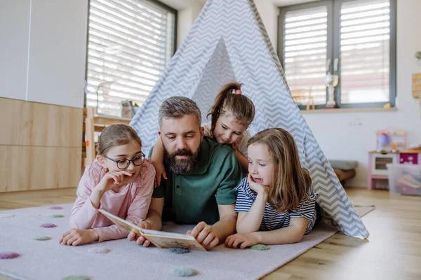 Ayah ceria dari tiga anak perempuan kecil membaca buku mereka di rumah. — Stok Foto