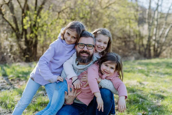 Батько з трьома маленькими доньками дивиться на камеру у весняній природі разом . — стокове фото