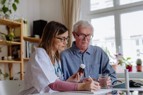 Trabalhador de saúde ou cuidador visitando o homem idoso dentro de casa, explicando a dosagem de medicamentos. — Fotografia de Stock