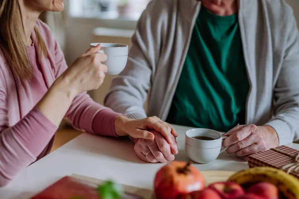 Vuxen dotter besöker sin äldre far hemma och dricker kaffe tillsammans, rör vid handen. — Stockfoto