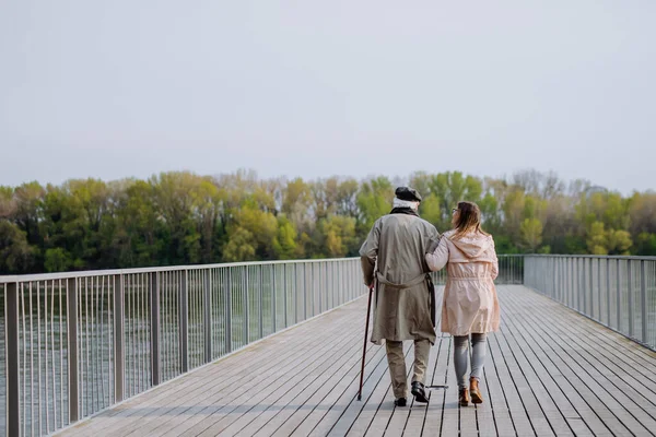 Rear view of senior man with daughter outdoors on a walk on pier by river. — стоковое фото