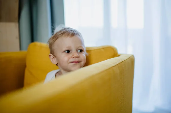 Liten nyfiken pojke sitter på soffan och tittar bort. — Stockfoto
