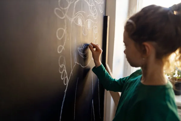 Little girl drawing with chalks on blackboard wall indoors in playroom. — 스톡 사진