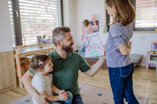 Father of three little daughters getting drawings from them at home. — Stockfoto