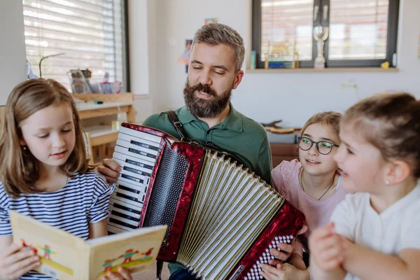 Radosny ojciec muzyk gra na akordeonie do swoich trzech córek w domu. — Zdjęcie stockowe