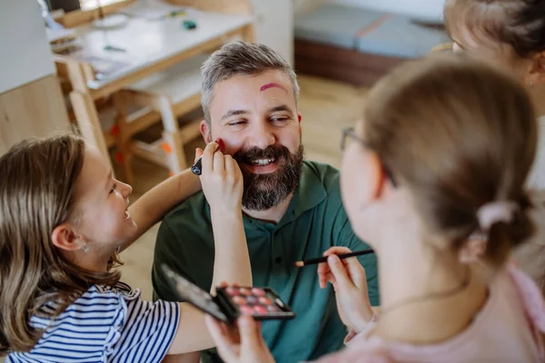 Three little girls putting on make up on their father, fathers day with daughters at home. — Stok fotoğraf