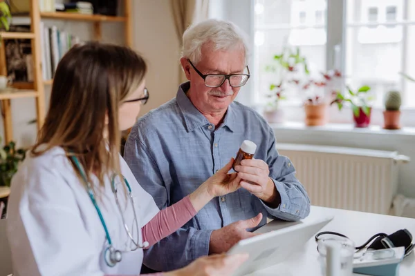 Healthcare worker or caregiver visiting senior man indoors at home, explaining medicine dosage. — Photo