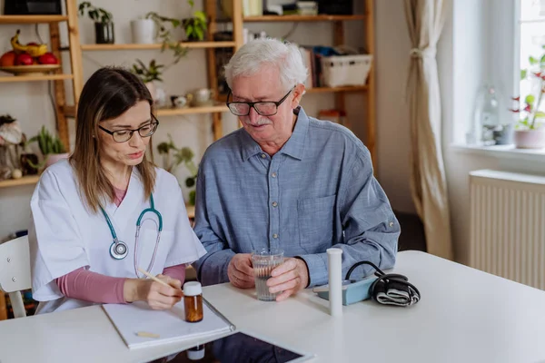 Healthcare worker or caregiver visiting senior man indoors at home, explaining medicine dosage. — Foto Stock