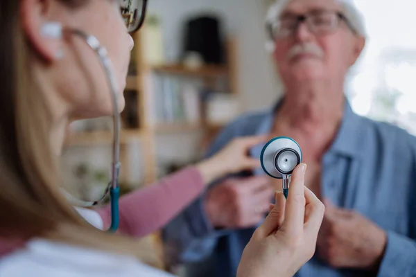 Female doctor visiting senior man and examinig him indoors at home. — Stok fotoğraf