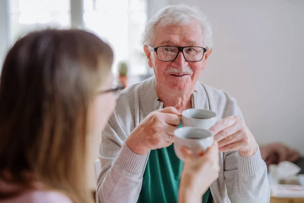 Adult daughter visiting her senior father at home and having coffee together, talking. — стоковое фото