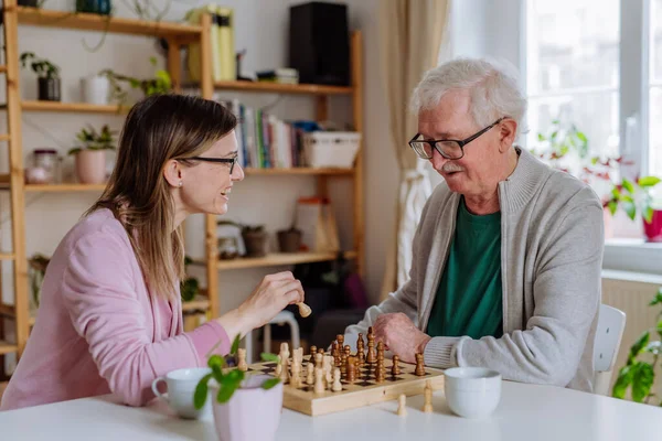 Filha adulta visitando seu pai sênior em casa e jogando xadrez juntos. — Fotografia de Stock