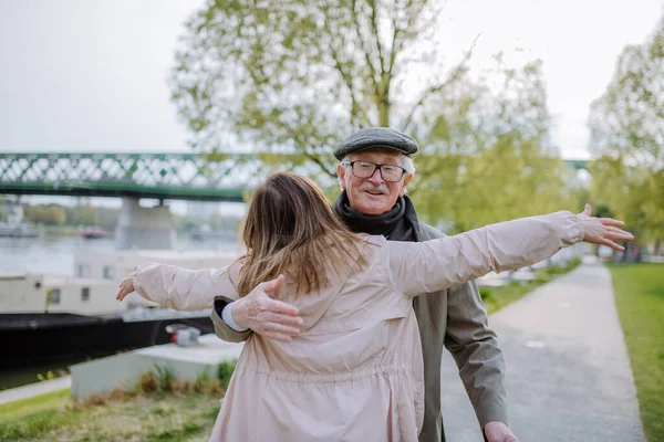 Rear view of adult daughter hugging her senior father when meeting him outdoors in street. — Foto de Stock