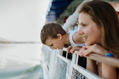 Little curious boy with his mother looking out from motor boat.