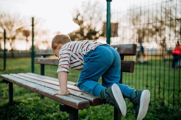 Little boy climbing up the bench on outdoor playground. — Fotografia de Stock