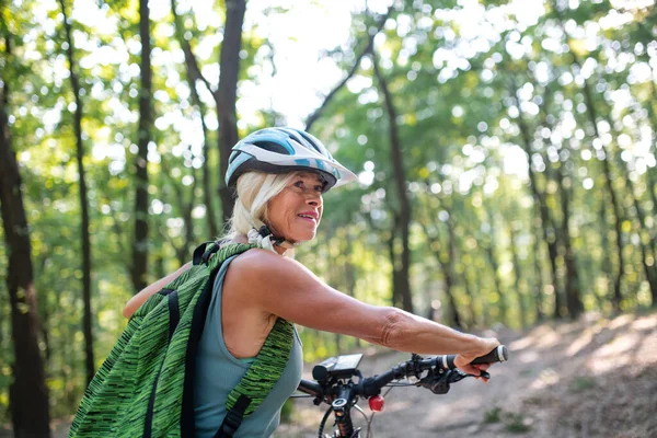 Aktywny starszy kobieta rowerzysta pchanie rower na zewnątrz w lesie. — Zdjęcie stockowe