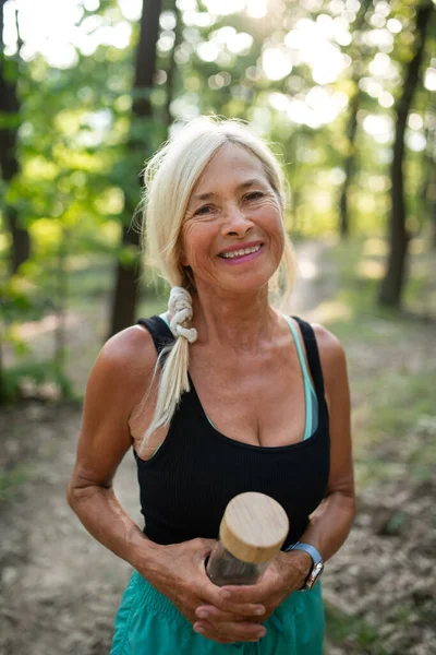 Retrato de mujer mayor activa corredora con botella de agua al aire libre en el bosque. — Foto de Stock