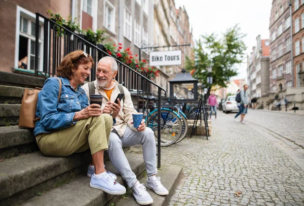 Счастливая пожилая пара туристов, сидящих на лестнице и увозящих кофе на открытом воздухе в городе — стоковое фото