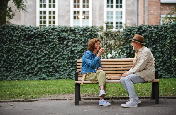 Happy senior couple sitting on bench and playing chess outdoors in park. — Stok fotoğraf