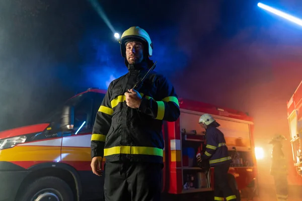 Low angle view of firefighter with fire truck in background at night. — Stock Photo, Image