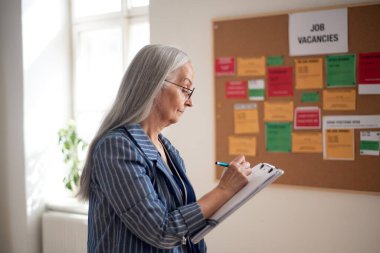 İş bulma kurumu çalışanı dosya formuyla iş ilanının önünde duruyor.