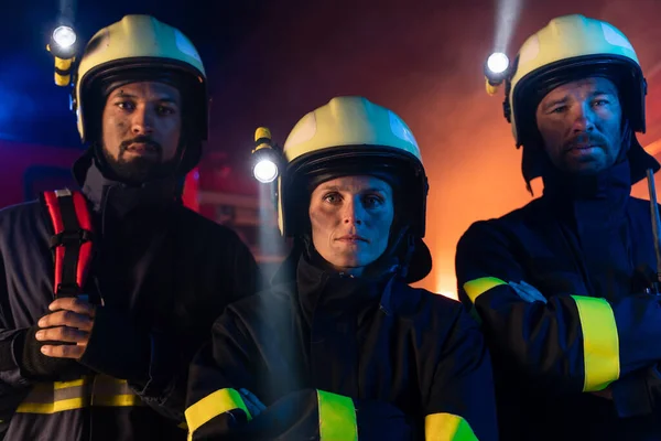 Firefighters men and woman at action with fire truck in background at night — Stock Photo, Image