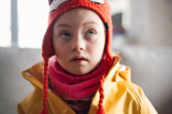 Niña con síndrome de Down mirando las salidas de la cámara en invierno contra la pared de ladrillo. —  Fotos de Stock