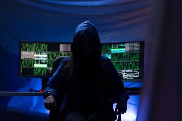 Hooded anonymous hacker by computer in the dark room at night, cyberwar concept. — Stock fotografie