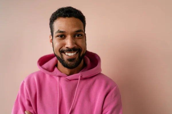 Fashion studio portrait of a young African American man in pink hoodie posing over beige background. — Stock Fotó