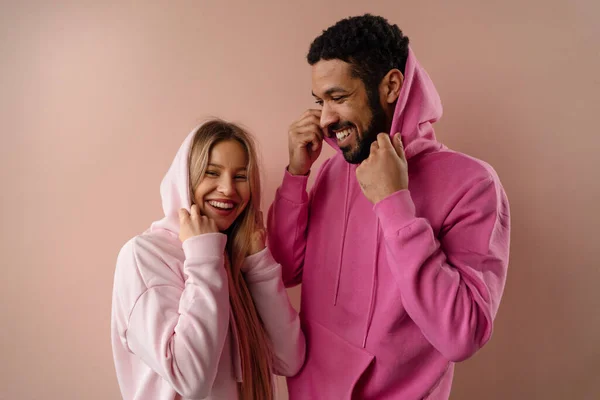 Modestudio Porträt eines glücklichen jungen Paares in Kapuzenpulli posiert vor rosa Hintergrund. — Stockfoto
