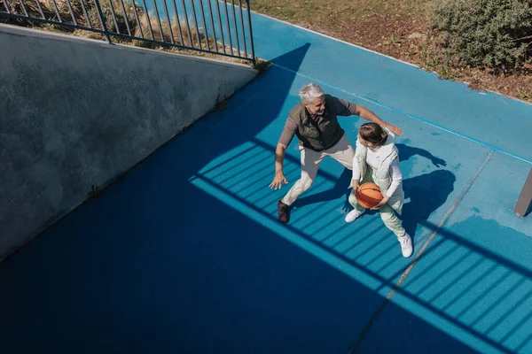 Father and teenage daughter playing basketball outside at court, high angle view. — Stock Photo, Image