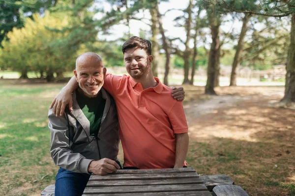 Glücklicher Senior-Vater mit seinem kleinen Sohn mit Down-Syndrom, der sich umarmt und im Park sitzt. — Stockfoto