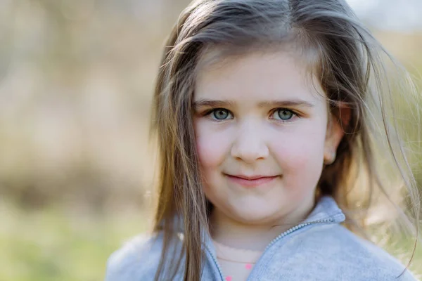 Un retrato de niña bonita de pie en el parque de verano mirando en la cámara sonriendo felizmente. — Foto de Stock