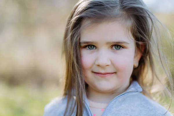 Un retrato de niña bonita de pie en el parque de verano mirando en la cámara sonriendo felizmente. —  Fotos de Stock