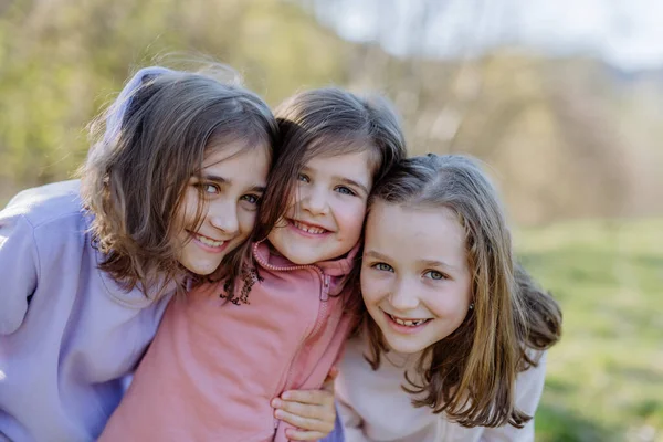 Tres hermanas pequeñas mirando a la cámara en la naturaleza de primavera juntas. —  Fotos de Stock