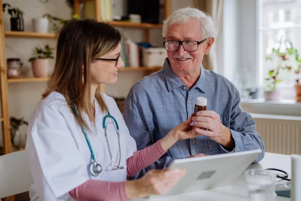 Healthcare worker or caregiver visiting senior man indoors at home, explaining medicine dosage. —  Fotos de Stock