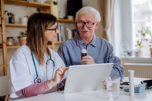 Healthcare worker or caregiver visiting senior man indoors at home, explaining medicine dosage. — Photo