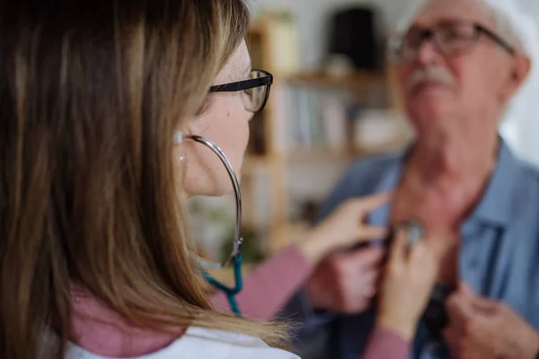 Médecin visitant l'homme âgé et l'examinant avec stéthoscope à l'intérieur à la maison, à l'écoute des battements de coeur. — Photo