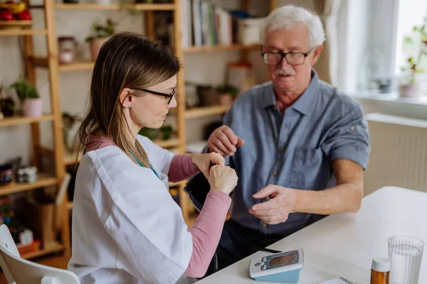 Žena lékař navštíví staršího muže a vyšetří ho doma, měření krevního tlaku. — Stock fotografie