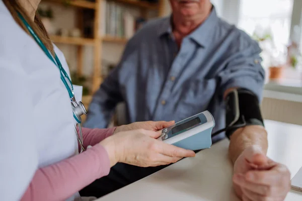 Doctora visitando a un hombre mayor y examinándolo en casa, midiendo la presión arterial. —  Fotos de Stock
