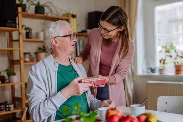 Happy woman surprising her senior father when visiting him at home and bringing present. — Stok fotoğraf